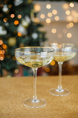Christmas festive decor. Beautiful glass glasses with champagne on golden background. Christmas tree. Winter holidays,