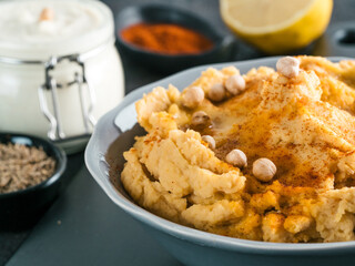 Homemade hummus with olive oil in gray bowl and ingredients. Traditional middle eastern appetizer hummus on gray background - healthy vegan paste snack. Vegetarian diet,nutrition protein food concept