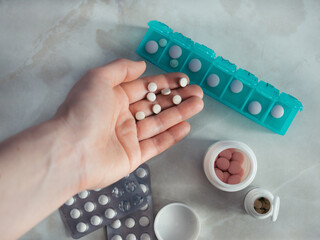 Hand with pills and pillbox. Top view of seven day pill box with pills. Green pill-box over light...