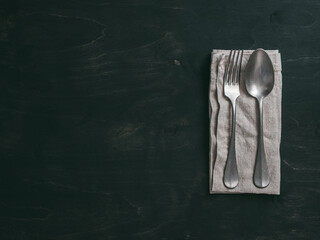 Vintage cutlery over dark background. Old tablespoon and fork on linen napkin over black table. Top view or flat-lay. Copy space for text.