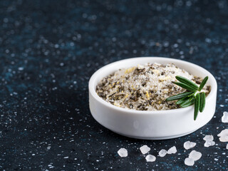 Sea salt scented herb rosemary and lemon zest. Sea salt with aromatic herbin small bowl on dark blue background. Scented salt and ingerdients. Copy space