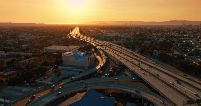 Busy interchange lit with orange light at sunset. Vast cityscape of Los Angeles, California, USA from top.