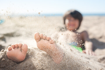 Close-up of a child's feet with sand from the beach falling on them to be buried.
