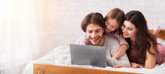 Family Rest. Young Parents And Their Little Daughter Using Laptop In Bed, Browsing Internet Or...