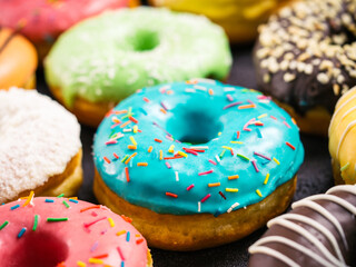 Close up view of assorted colorful donuts on dark background. Focus on blue glazed doughnut with...