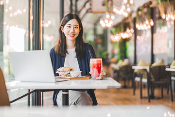 Happy asian woman healthy eating breakfast sandwich at cafe sitting near window indoors on day