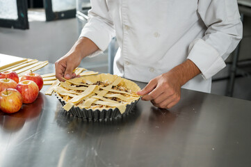 Pastry chef decorates an apple pie by adding strips of uniform dough.