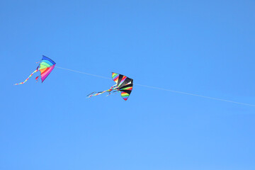 Two multicolored large kites flying high in the blue sky symbolizing childhood and lightheartedness