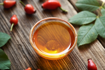 A bowl of rosehip seed oil with fresh rose hips on a table
