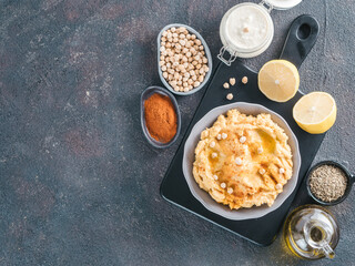 Homemade hummus in gray bowl and ingredients. Traditional middle eastern appetizer hummus on dark background - healthy vegan paste snack. Vegetarian diet,nutrition protein food concept. Copy space.