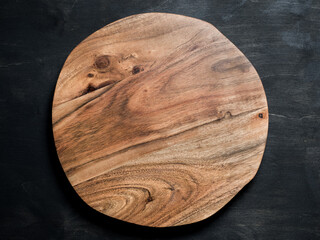 Round wooden tray or cutting board on black table. Top view of empty kitchen trendy rustic wooden...
