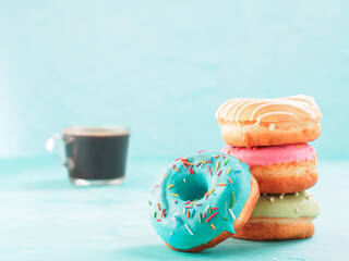Donuts and coffee on blue concrete background with copy space. Colorful donuts and coffee cup with copyspace. Glazed doughnuts in stack on foreground and coffee on background