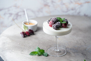 Delicious italian dessert panna cotta with iced berries and mint on light background.