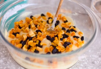 Gluten free dough with piece of dried fruits in it in a glass bowl on a kitchen table