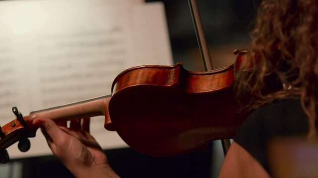 Closeup shot of female violin musician reading a note and playing a symphony.