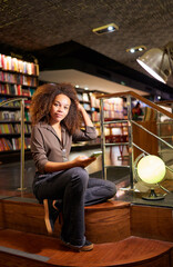 Young black woman sitting on library steps holding cell phone 