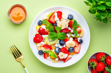 Fruit and berry salad with ricotta and honey, green background, top view