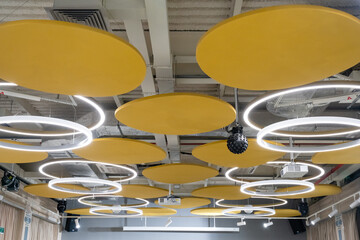 This contemporary ceiling design features elegant circular lights complemented by acoustic panels, all adorned in a vibrant shade of yellow