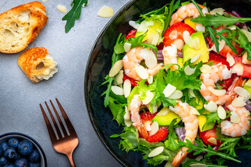Foodie food salad with shrimp, strawberries, onion, arugula and almond petals, gray background, top
