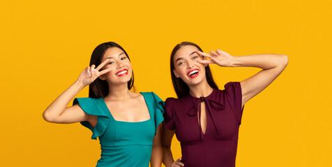Fototapeta na wymiar Three Multiracial Girlfriends In Evening Dresses Having Fun Posing Over Yellow Background. Studio Shot
