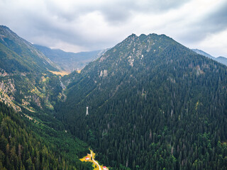 Aerial view of green mountains with a winding road and dramatic cloudy skies above.