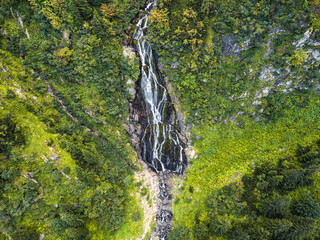 Aerial drone view of a majestic waterfall cascading down rocky cliffs, surrounded by lush greenery.