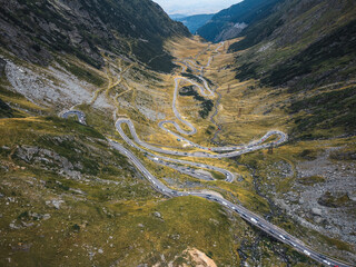 Drone view of the Transfagarasan highway in autumn, showcasing vibrant fall colors and cars winding along the road.