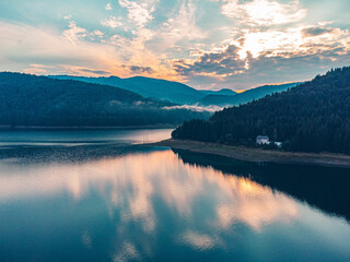 Aerial drone view of a serene lake at sunset, framed by majestic mountains and vibrant sky colors.