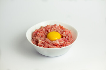 Shredded pork (mince) with a raw egg in the middle in a white bowl on a white background.