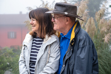 Portrait of smiling senior couple outdoors on a foggy day looking away smiling. Retired seniors enjoying nature and healthy lifestyle on vacation or retirement