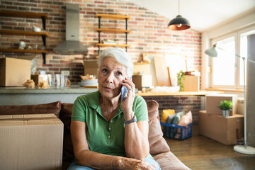 Senior woman on phone while labeling moving boxes in new home