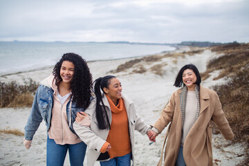 Three diverse young female friends walking on the beach in winter