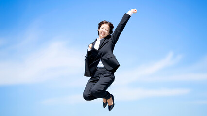 青空にジャンプする就職生・新入社員の女性