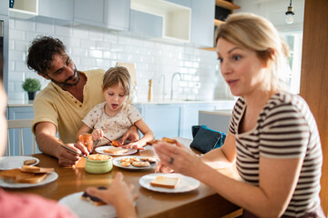 Family having breakfast together in kitchen with parents and child making toast