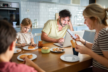 Father working on laptop while family has breakfast in kitchen