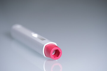 A pen injector with a red tip for biological treatments such as Adalimumab, Etanercept or epinephrine. The background is aseptic, clean, white and well lit.