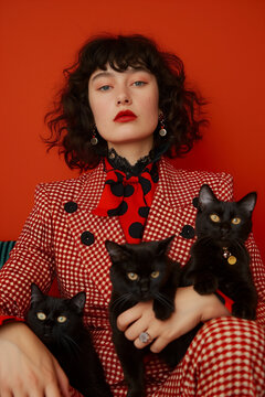 Stylish childless cat woman with two black cats posing in a red studio with a third cat nearby