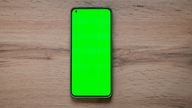 top view of a phone with a green screen on a wooden table