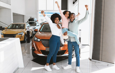 Full length of excited African American family lifting hands up, celebrating new car purchase at...