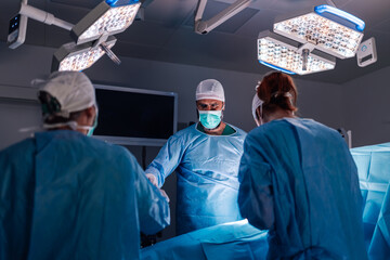 Team of surgeons working precisely under operating room lights.