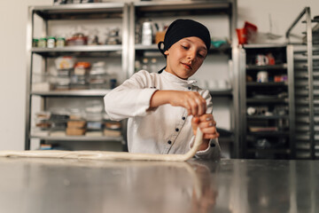 Focused young girl chef twisting pastry dough in modern professional kitchen.