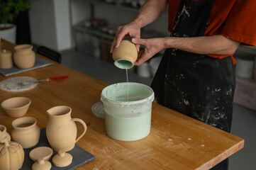 Close-up of a potter's hands glazing a pottery piece. 