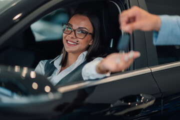 Woman smiling, reaches for car keys handed over by another in a dealership