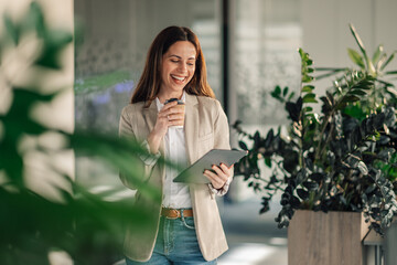 Happy smart casual businesswoman with tablet drinking coffee at office