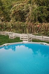 A frame pool filled with water in an early autumn garden. Swimming pool on a green lawn.