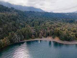 Aerial View of Cultus Lake, BC, Canada Coastline Showing Turquoise Water with people picnicking and swimming on a holiday. Cloudy day with sun rays shining onto water. Summer turning to Autumn.
