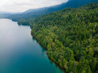 Aerial View of Cultus Lake, BC, Canada Coastline Showing Turquoise Water with Trees and Mountains on a Cloudy Day. Summer day with trees starting to turn yellow for fall.