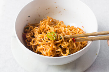 Overhead view of Spicy instant noodles with slices of green and red chili, spicy ramen noodles in a white ceramic bowl