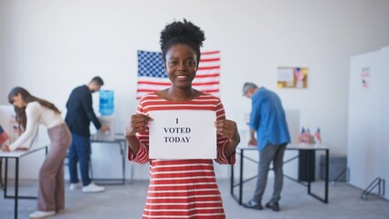 Camera moving away from beautiful African American woman holding sign stating that she voted today. Motivating others to complete their duty and take part in presidential elections.