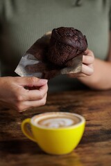 Portrait of a young woman holding a chocolate muffin in her hands and a coffee to accompany and dip it in. Delicious breakfast or snack. Craving something sweet. Sugar cravings. Homemade muffins.